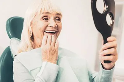 woman looking in the mirror in awe after her restorative dentistry procedure